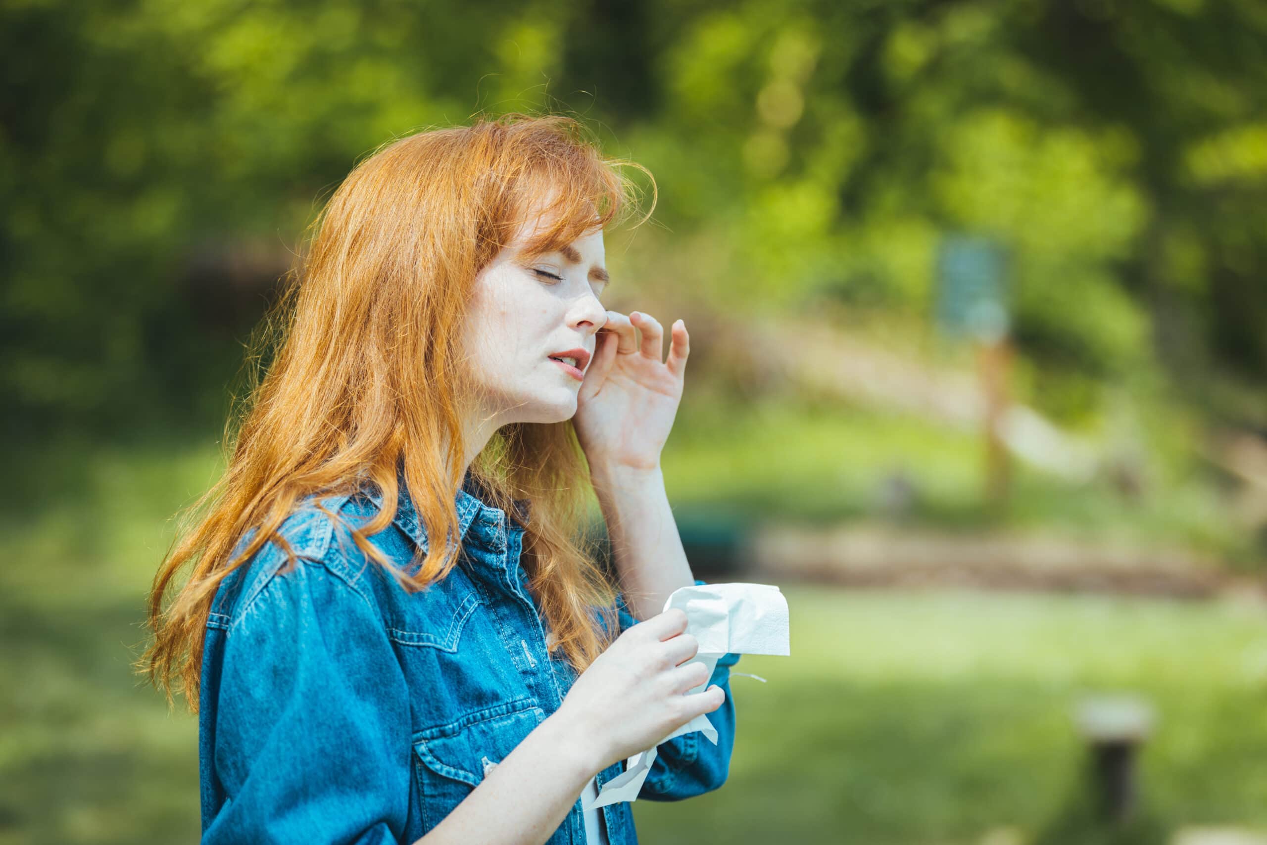 Young Woman Sneezing In Park. Allergy, Flu, Virus Concept. Spring Allergy Concept. Young Woman Suffering From Allergy Outdoors. Young Woman With Pollen Allergy